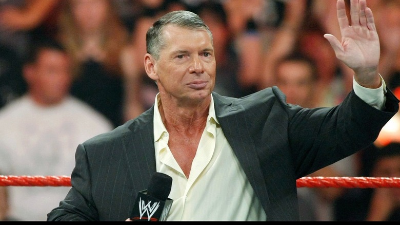 Vince McMahon waves his hand as he stands in a WWE ring.