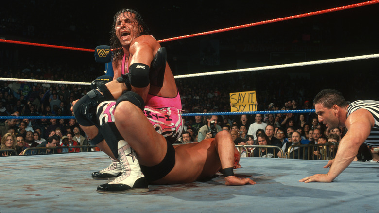 Bret Hart with Steve Austin in Sharpshooter while referee Ken Shamrock checks on him at WWE WrestleMania XIII