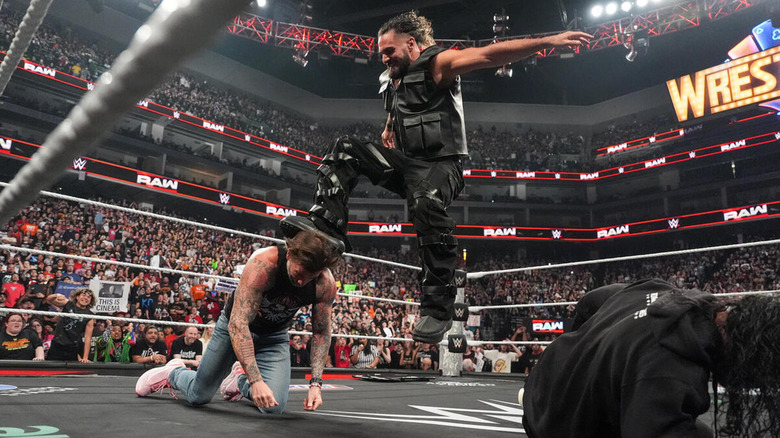 Seth Rollins stomps CM Punk while a downed Roman Reigns watches.