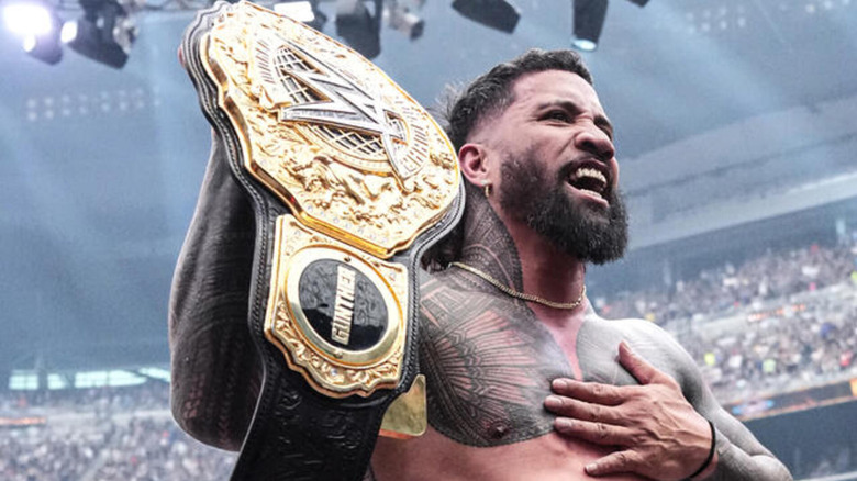Jey Uso pats his chest as he holds the WWE World Heavyweight Championship.