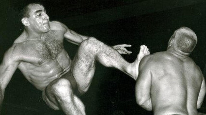 Antonio Rocca hits an opponent with a dropkick from the top turnbuckle in the ring during a match.