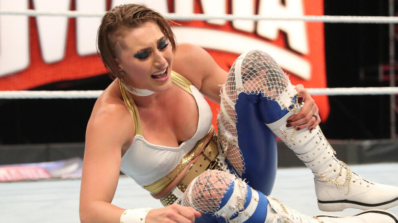 Rhea Ripley sits grasping her knee in the middle of the ring during her WrestleMania WWE NXT Women's Championship match against Charlotte Flair.