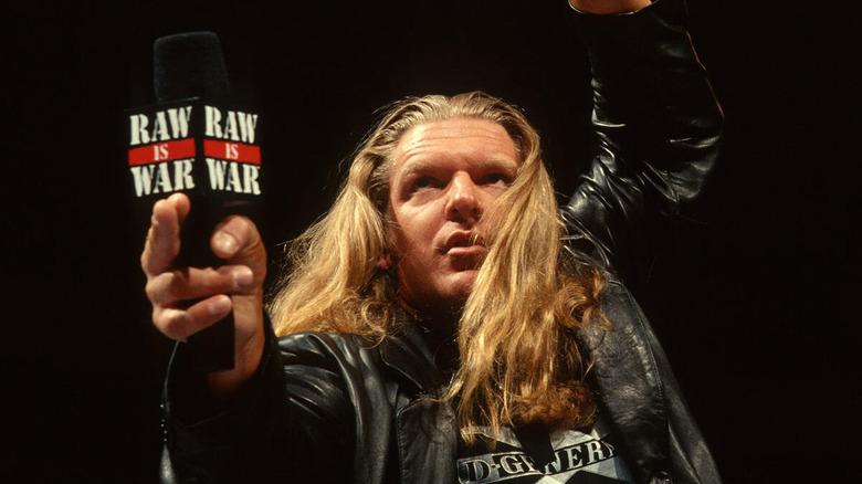 Triple H poses in the ring with a microphone with a "Raw is War" microphone flag during an episode of "WWE Monday Night Raw."