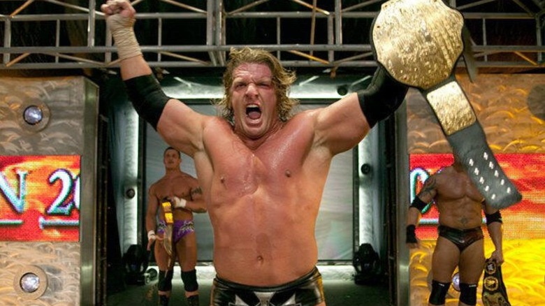 Triple H holds up the World Heavyweight Championship on stage flanked by Randy Orton and Batista after a match.