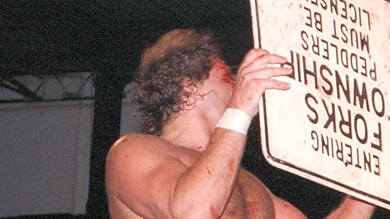 A bloody Tracy Smothers shields himself with a sign at an ECW event