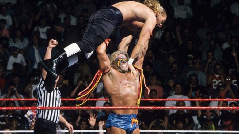The Ultimate Warrior lifts Hunter Hearst Helmsley over his head before slamming him to the mat during their match at WrestleMania 12.
