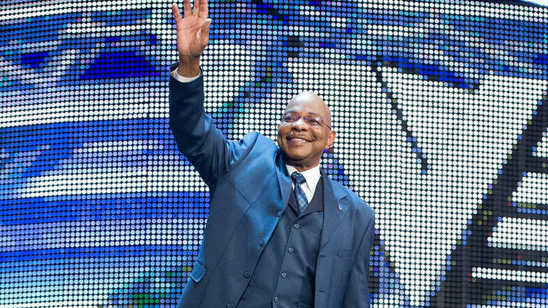 Theodore "Teddy" Long smiles and looks to the crowd from the stage during an episode of "WWE SmackDown."