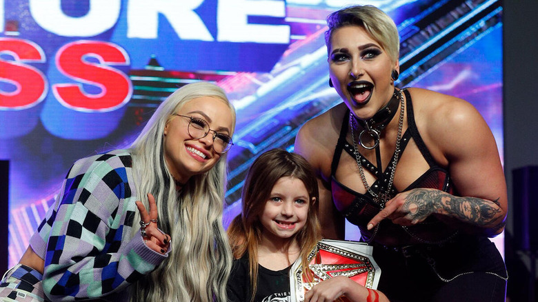 Liv Morgan and Rhea Ripley greet a young fan during an event at the WrestleMania Axxess Store.