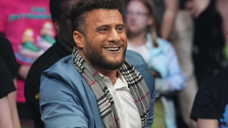 MJF stands smirking behind the ring barricade, looking on to the ring at the Hurt Syndicate in action during AEW Dynasty.